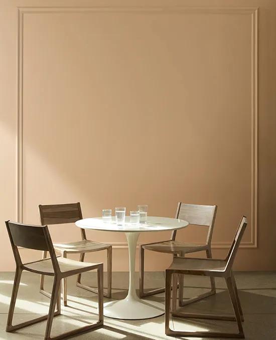 A light brown painted dining room wall with hints of golden yellow and picture frame wall molding pairs beautifully behind a white tulip table and wood chairs.