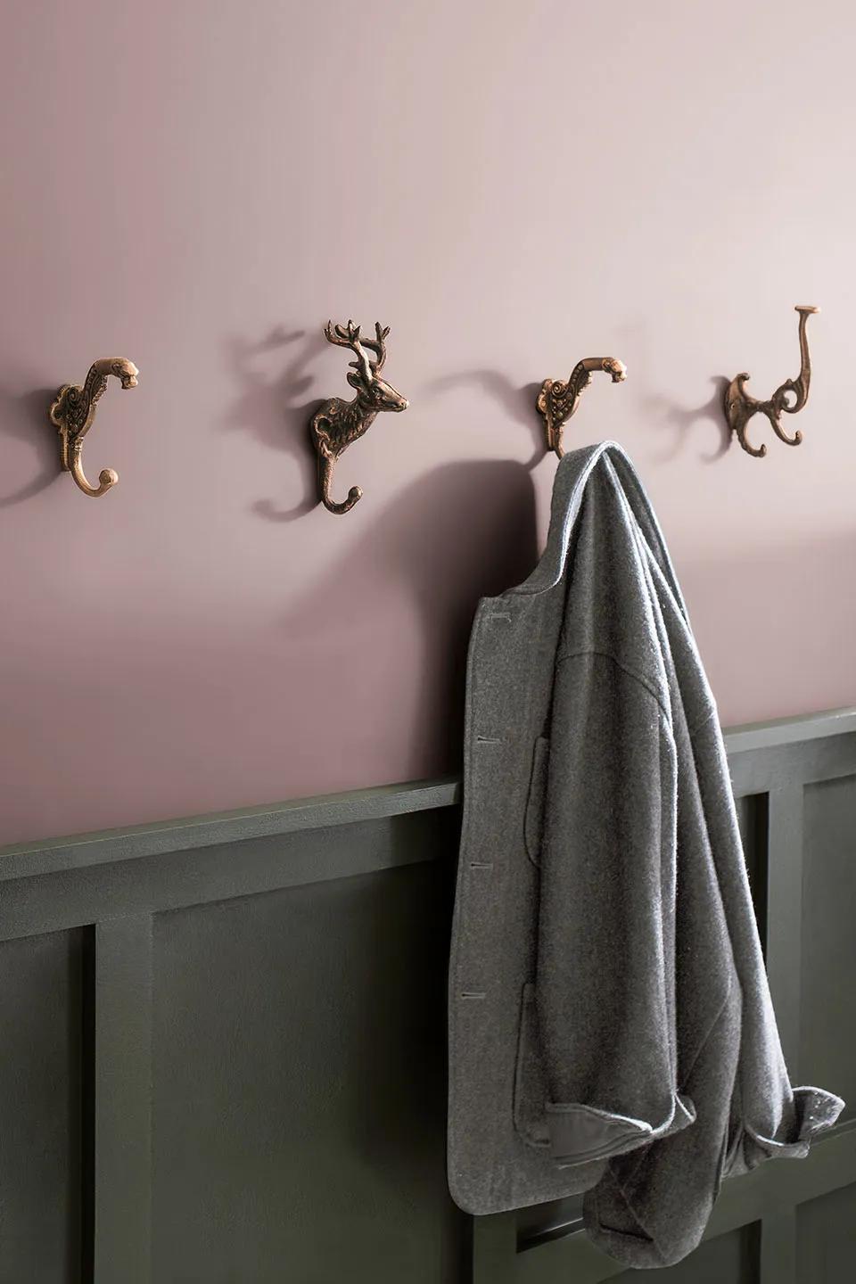 A gray blazer hangs from a whimsical gold coat hook in an entryway with purple walls and green wainscoting