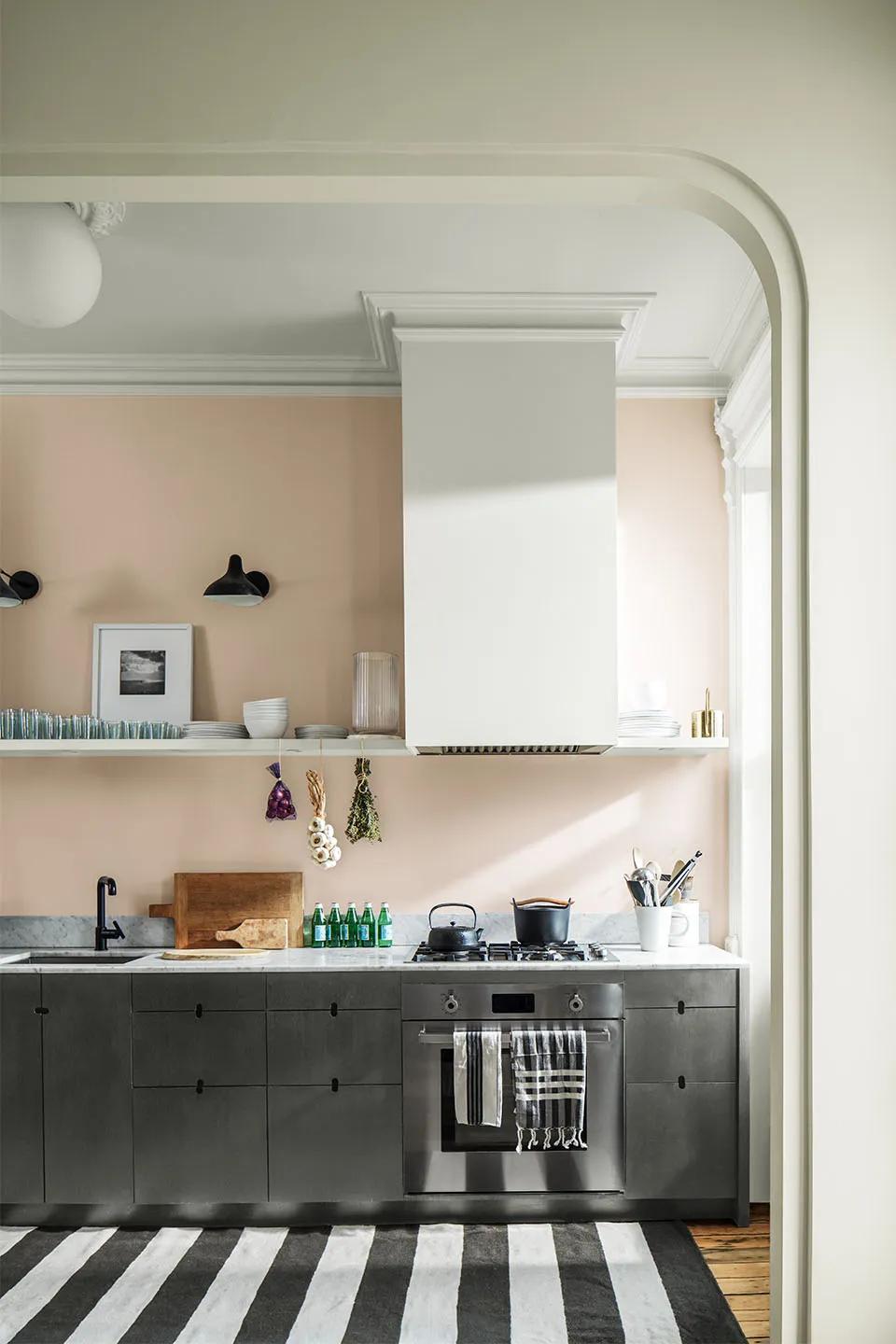 Una cocina moderna con paredes en rosa claro, gabinetes oscuros y una alfombra rayada de color blanco y negro.