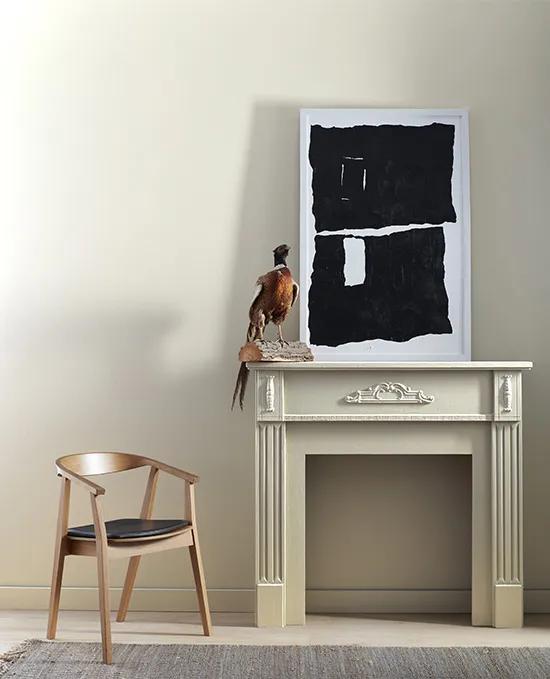 A light gray painted mantel and wall complements a framed black and white abstract art piece and modern wood chair with a black seat.